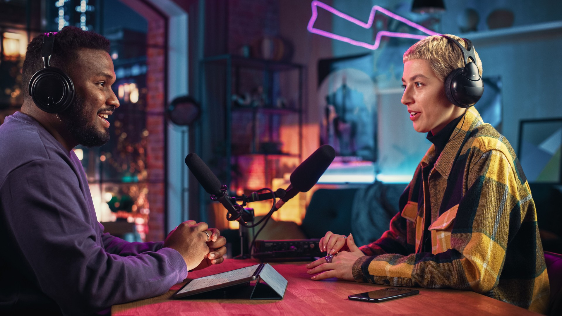 Two Young Stylish Radio Show Hosts Record Fresh Podcast Episode in Home Loft Studio Apartment. Attractive Energetic Co-hosts Discuss Important Topics Live on Air in an Evening Show.